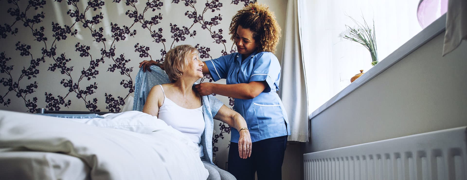 a caregiver assisting senior woman dressing in her bed